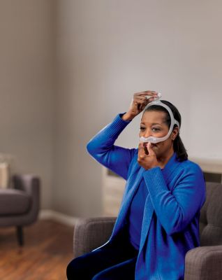 Woman in blue sweater putting on mask.