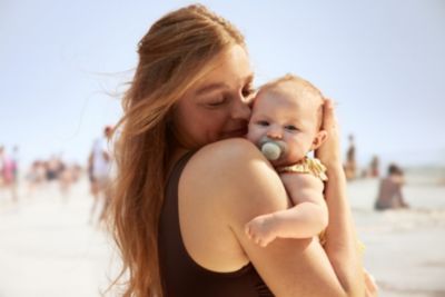 Elternteil hält ein Baby mit Schnuller am Strand