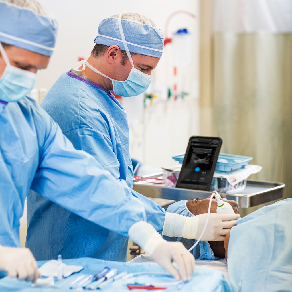 Patient in anesthesia setting with clinicians consulting mobile ultrasound system