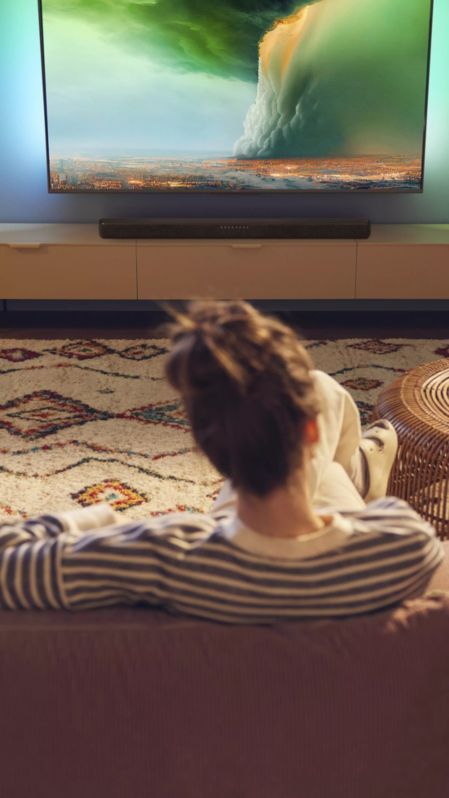 Person watching Philips Ambilight TV with a soundbar in a cozy living room