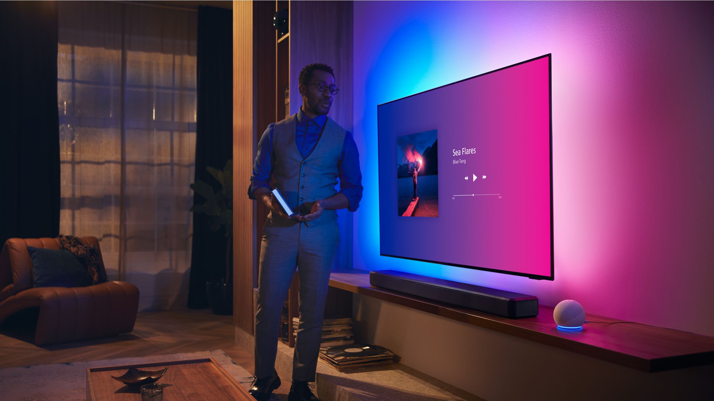 Person in a modern living room near a Philips Ambilight TV with music interface and Fidelio soundbar