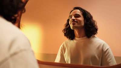 Een man met een zieleplek glimlacht terwijl hij naar zichzelf kijkt in een grote ronde spiegel.