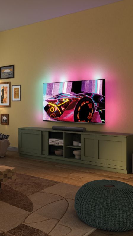 A person relaxes in front of an Ambilight TV, with a soundbar below