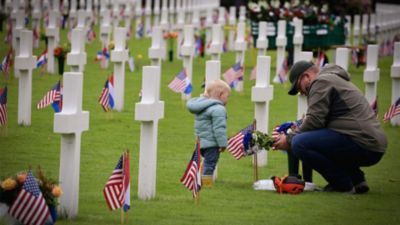 Man and young child placing flowers at white cross grave markers with American flags