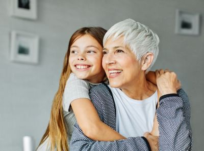 Mujer mayor y niña sonriendo mientras se abrazan en interiores