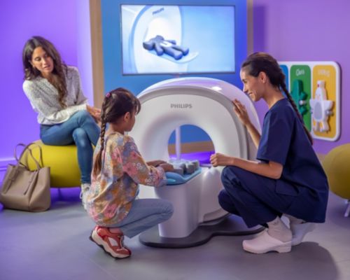 Manipulatrice en électroradiologie médicale interagissant avec un enfant qui utilise le Kitten Scanner avant un examen IRM