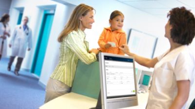 Patient with child interacting with hospital receptionist at front desk using digital system