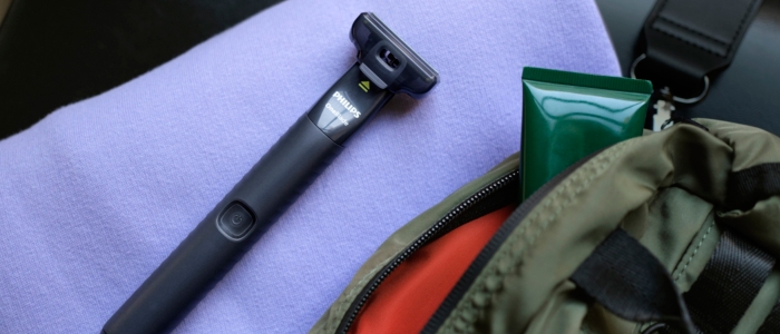 The portable shaver, OneBlade, sits on top of a towel, next to a travel bag.