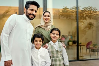 عائلة مكوّنة من أربعة أفراد تبتسم وتقف أمام منزل حديث