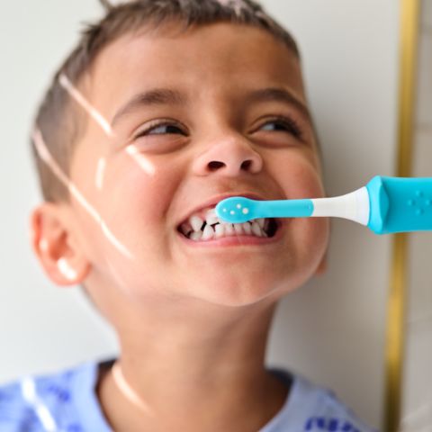Girl showing off her smile while holding a Sonicare For Kids power toothbrush