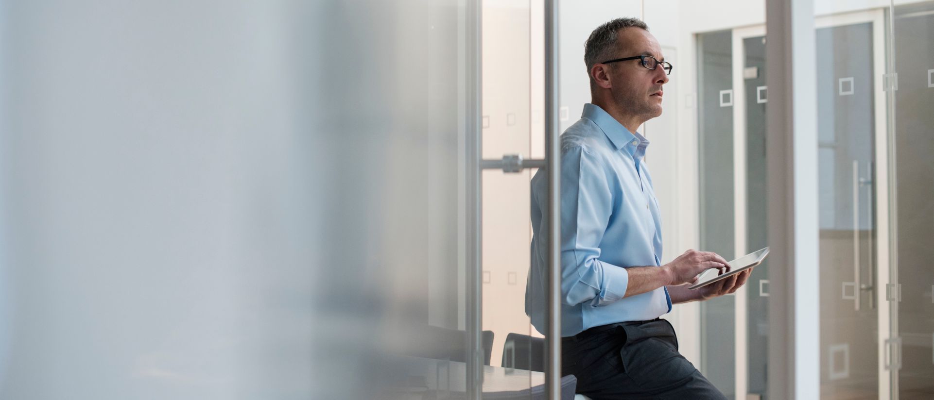 businessman leaning against desk looking at tablet