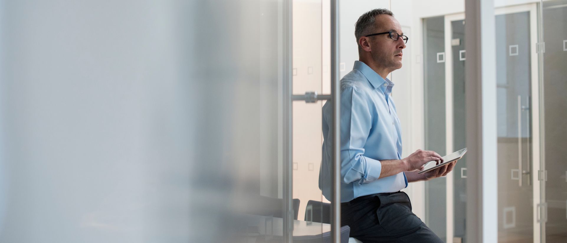 businessman leaning against desk looking at tablet