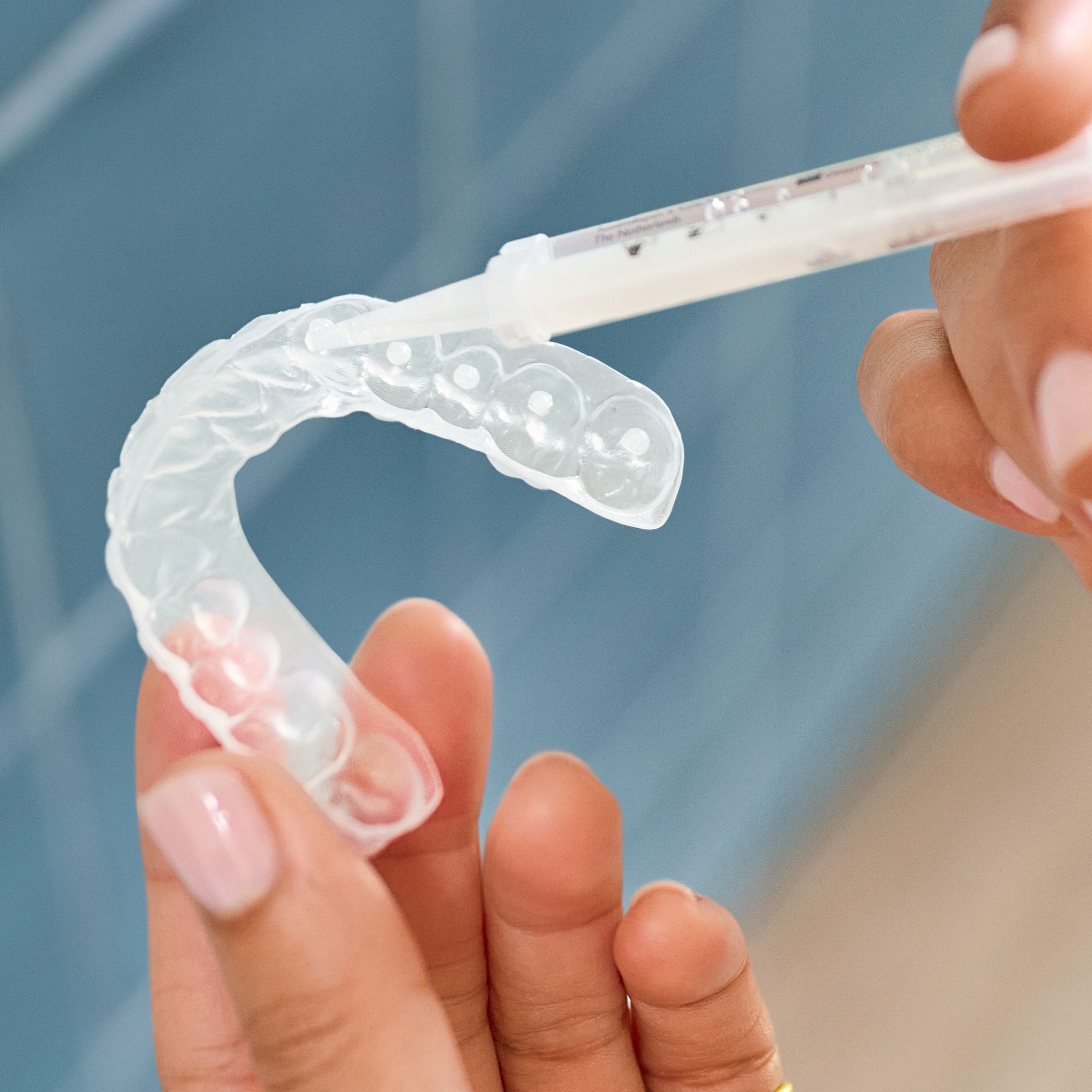 A hand filling a whitening tray with gel.