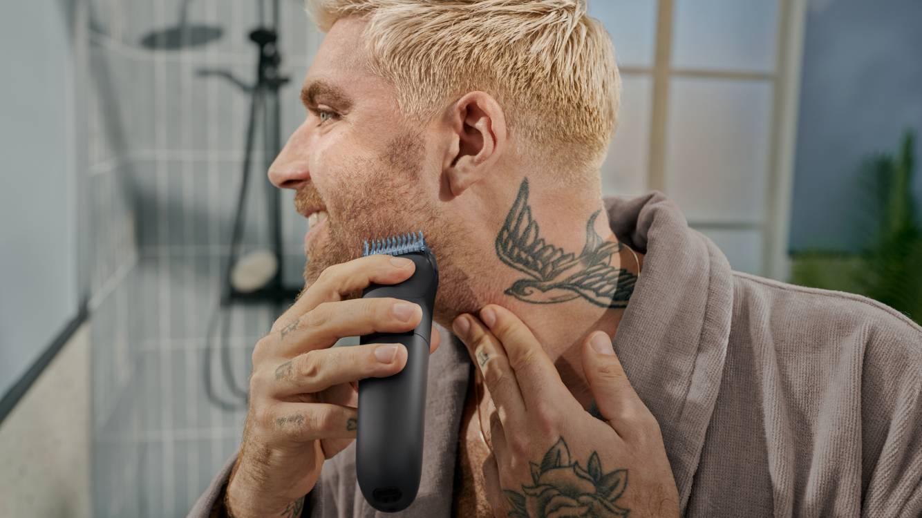 Ein blonder Mann mit einem Vogel-Tattoo im Nacken rasiert seinen Bart mit dem Philips OneBlade. 
