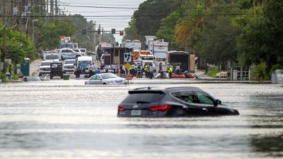 Flooded street with submerged cars and emergency responders in background