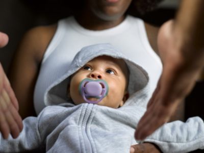 Das Baby trägt einen Kapuzenanzug mit Schnuller, während es gehalten wird