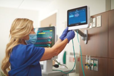 Enfermeira ajustando dispositivo de monitoramento de paciente Philips à beira do leito em quarto de hospital