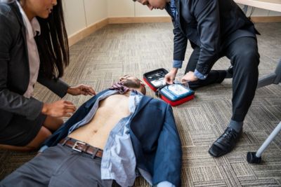 Colleagues using Philips HeartStart HS1 AED to assist person during cardiac emergency in office