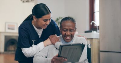 Caregiver assisting an older woman using a tablet at home