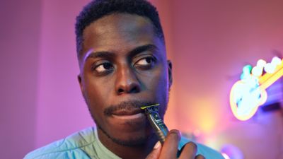 Een man vormt zijn snor met een Philips OneBlade, verlicht door een neonlicht op de achtergrond.