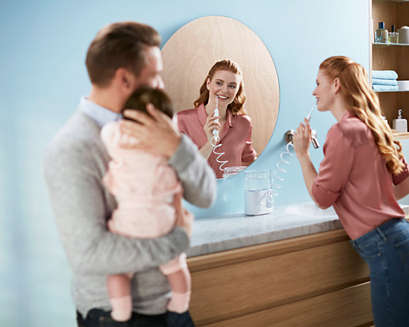 Man holding sleeping baby while woman uses a Power Flosser