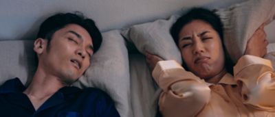 いびきをかく男性と枕で耳を覆う女性がベッドにいるカップル