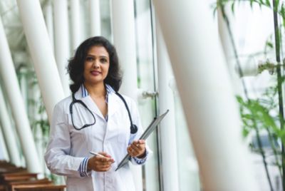 A healthcare professional in a white lab coat stands in a bright, modern corridor