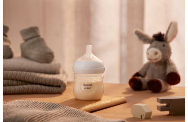 Product image of a Philips Avent Natural Response baby bottle in front of a toy donkey on a wooden surface.
